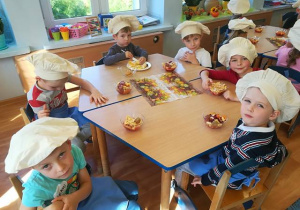 Dzieci przy stolikach prezentują wykonane owocowe desery.